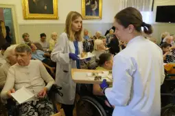 Młoda osoba serwująca jedzenie w sali z seniorami.