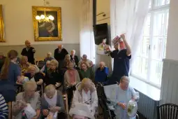 Spotkanie seniorów w sali, rozdawanie paczek z jedzeniem.