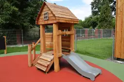 Drewniany plac zabaw z domkiem i zjeżdżalnią na kolorowej nawierzchni.