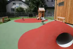 Plac zabaw z drewnianą konstrukcją, zjeżdżalnią i kolorową nawierzchnią.
