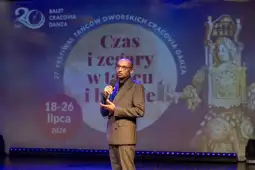 Mężczyzna z mikrofonem na tle plakatu festiwalu tańca.