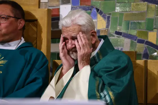 Starszy mężczyzna w szatach liturgicznych, z rękami na twarzy, wyraża emocje.