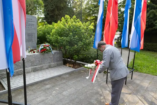 Mężczyzna składa wieniec przy pomniku, otoczony flagami.
