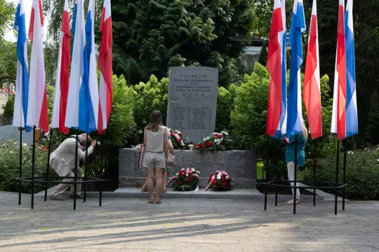 Pomnik z flagami i kwiatami, ludzie składający hołd.
