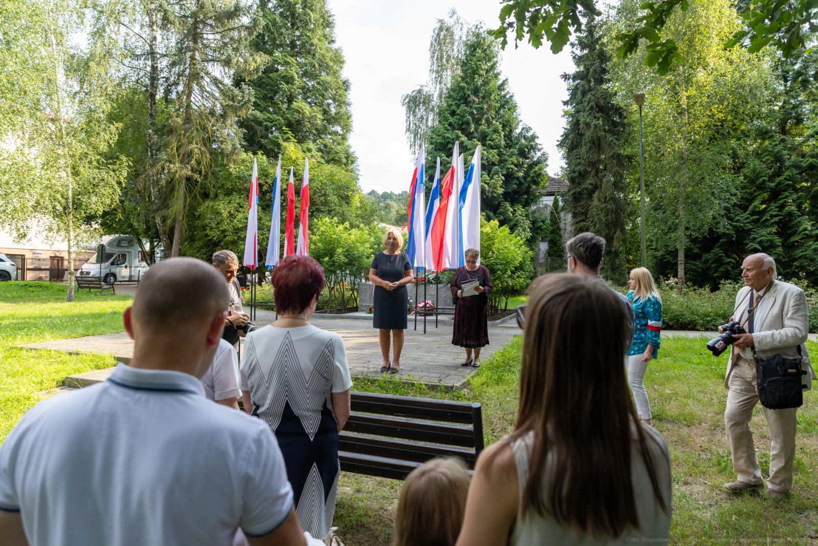 Uroczystość z flagami, przemawiająca kobieta i zgromadzenie osób w parku.  Autor: Bogusław Świerzowski