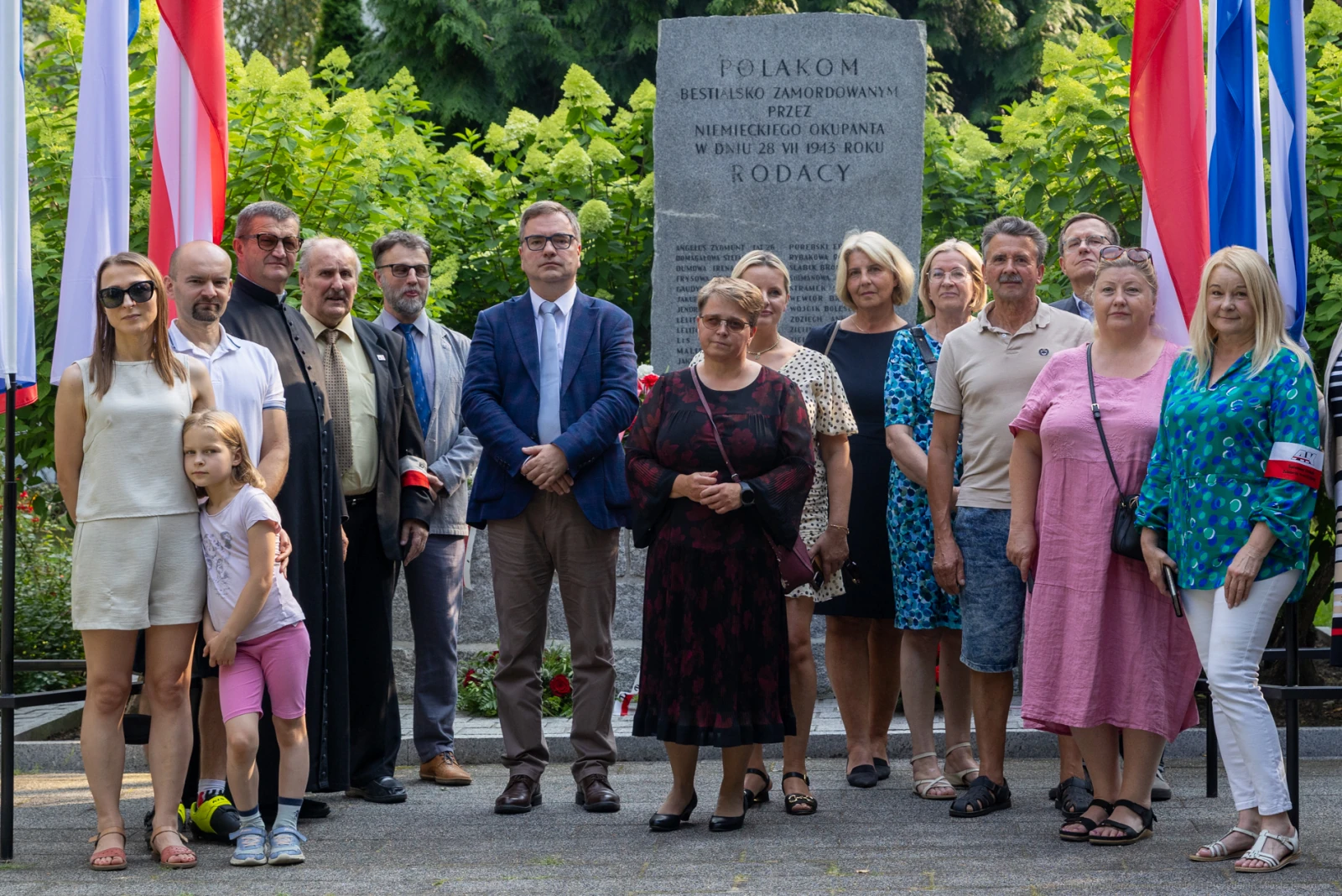 Grupa ludzi stojąca przy pomniku, z flagami w tle, podczas uroczystości upamiętniającej.  Autor: Bogusław Świerzowski