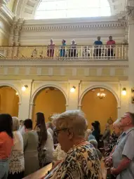 Ludzie modlący się w kościele, niektórzy na balkonie, inni w głównej części.