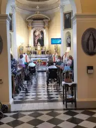Wnętrze kościoła z osobami w wózkach inwalidzkich, ołtarz i kwiaty.