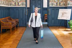 Kobieta w eleganckim stroju idzie korytarzem, trzymając torbę w ręku.