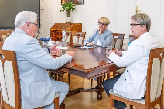 Spotkanie trzech osób przy stole w biurze, omawiają sprawy biznesowe.