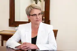 Kobieta w okularach, w białym garniturze, siedzi przy biurku w biurze.