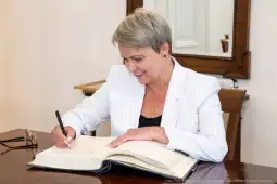 Kobieta w białym żakiecie podpisuje dokument w eleganckim wnętrzu.