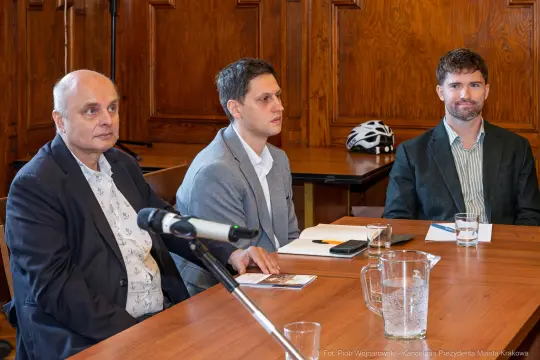 Trzech mężczyzn siedzących przy stole w sali konferencyjnej.