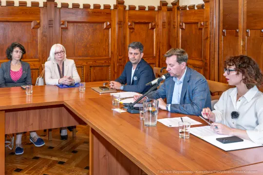 Spotkanie grupy ludzi przy stole, dyskusja w formalnym otoczeniu.