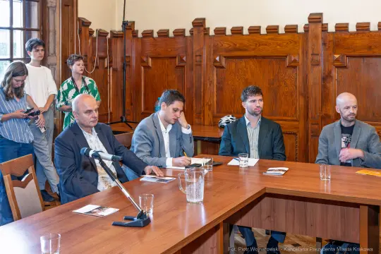 Spotkanie w sali z pięcioma mężczyznami przy stole, w tle obserwatorzy.