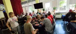 Grupa ludzi siedzących przy stołach w jadalni, jedzących posiłki i rozmawiających.