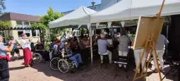 Spotkanie osób starszych w ogrodzie, z występem artystycznym i publicznością.