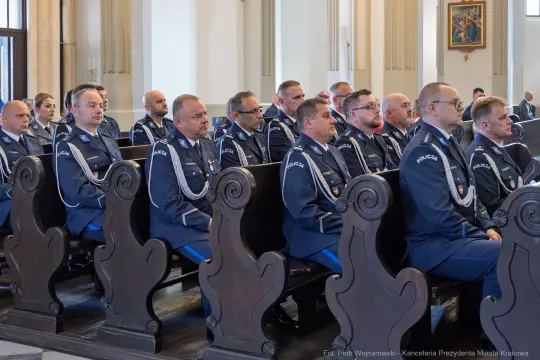 Uroczystość z udziałem mundurowych w sali z ławkami i dekoracjami.