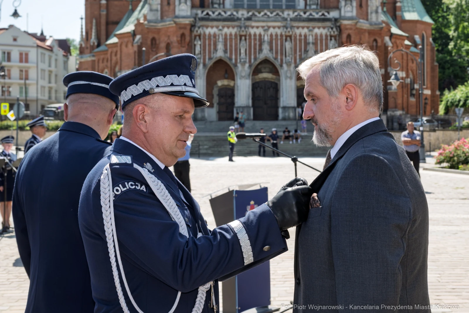 Ceremonia wręczenia odznaczeń przez policjanta mężczyźnie w garniturze przed budynkiem.  Autor: Piotr Wojnarowski