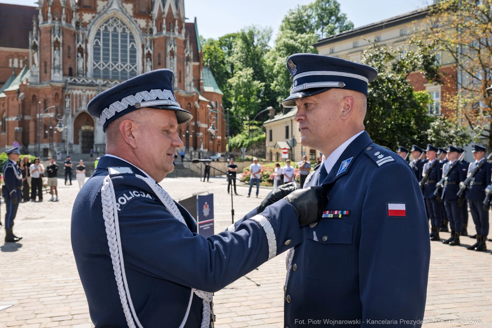 Ceremonia wręczenia odznaczenia policjantowi na tle budynku.  Autor: Piotr Wojnarowski