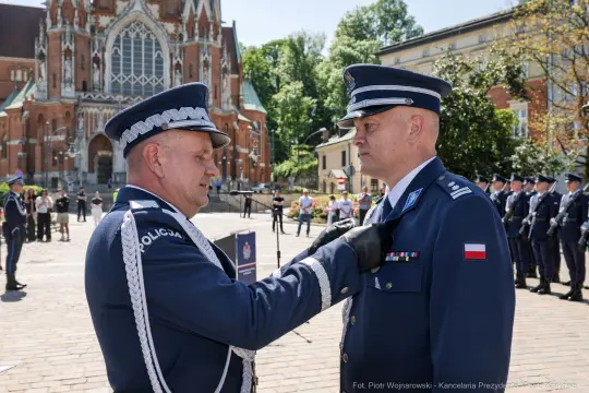 Ceremonia wręczenia odznaczenia policjantowi na tle budynku.