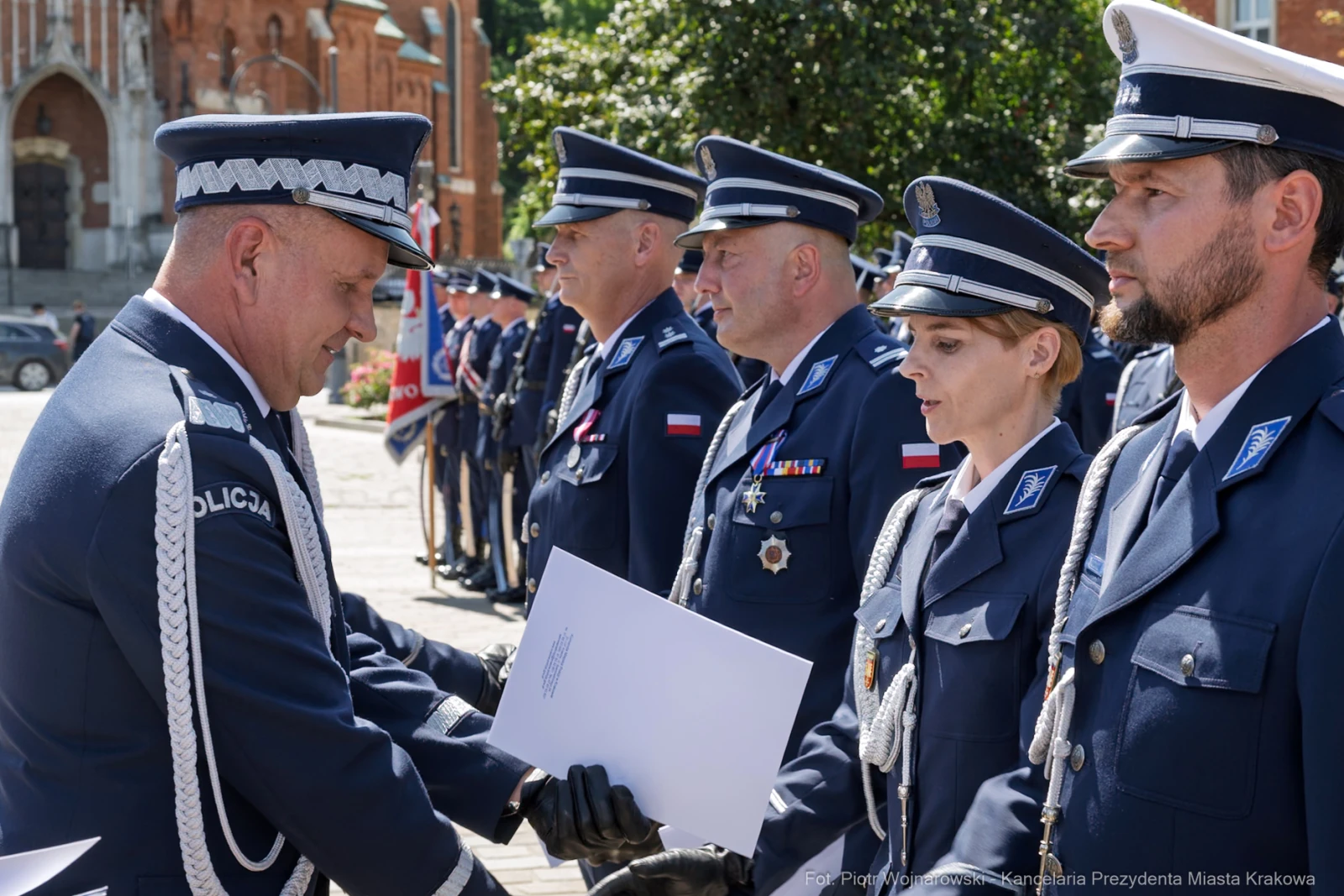 Ceremonia wręczenia odznaczeń policjantom w mundurach na tle budynków.  Autor: Piotr Wojnarowski