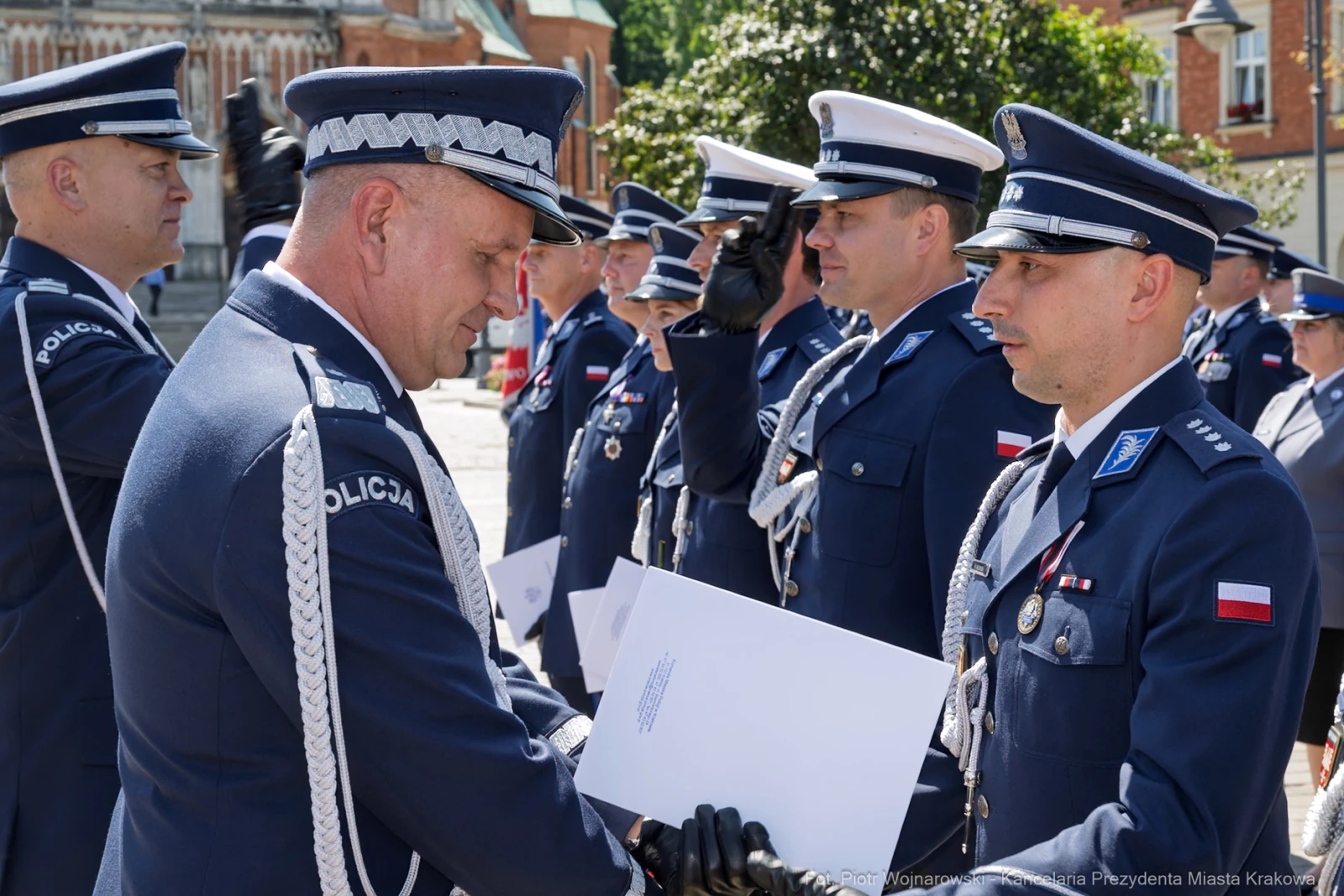 Ceremonia wręczenia odznaczeń policjantom w mundurach na tle budynków.  Autor: Piotr Wojnarowski