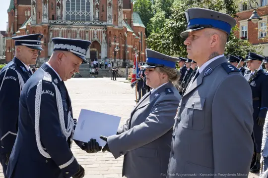 Ceremonia wręczenia odznaczeń policjantom przed budynkiem w tle.
