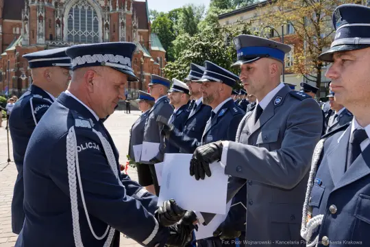 Ceremonia wręczenia odznaczeń policjantom w otoczeniu budynków i drzew.
