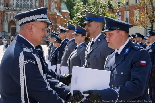 Ceremonia wręczenia dokumentów przez policjantów w mundurach na tle architektury.