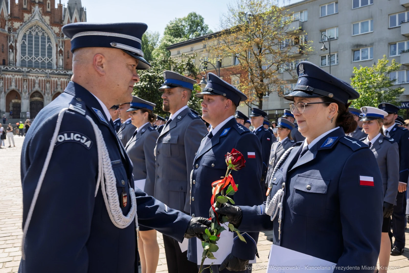 Ceremonia wręczenia kwiatów przez policjantów na tle budynków.  Autor: Piotr Wojnarowski