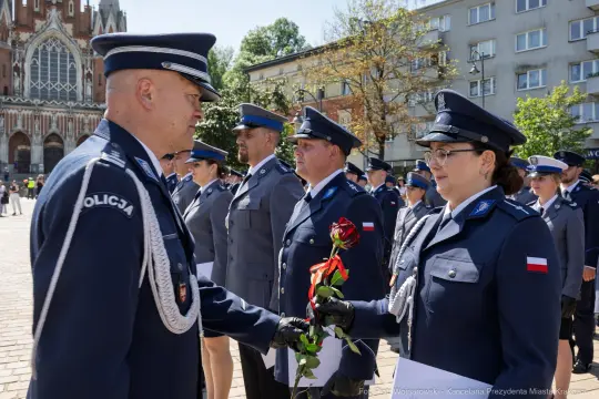 Ceremonia wręczenia kwiatów przez policjantów na tle budynków.