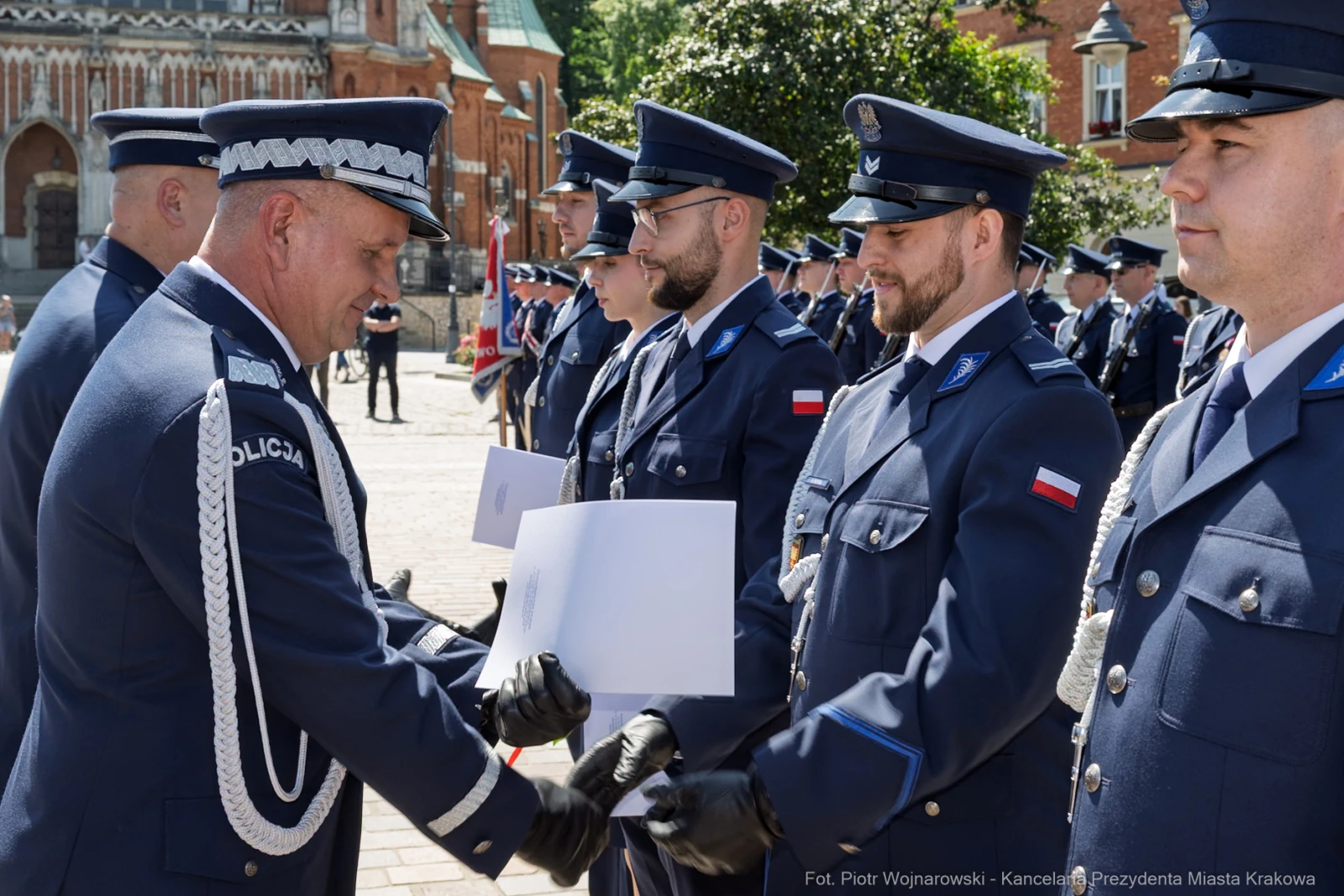 Ceremonia wręczenia odznaczeń policjantom w mundurach na tle budynków.  Autor: Piotr Wojnarowski