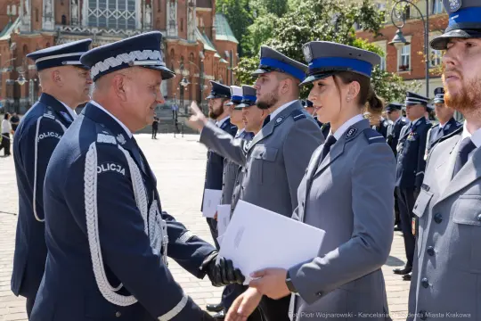 Ceremonia wręczenia dyplomów policjantom w mundurach na tle budynku.