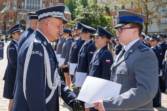 Ceremonia wręczenia dyplomów policjantom w mundurach, z flagami Polski w tle.