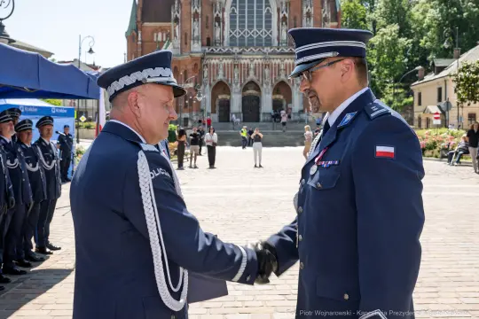 Ceremonia wręczenia odznaczeń w tle katedry, dwóch mężczyzn w mundurach w uścisku dłoni.