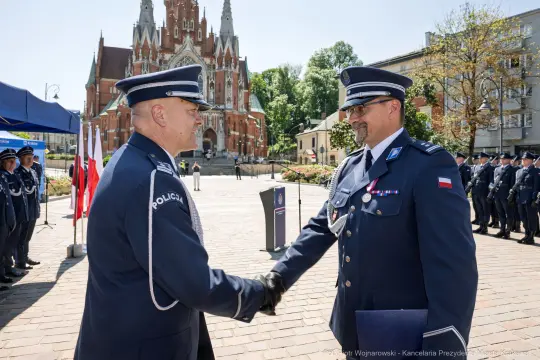 Ceremonia wręczenia odznaczeń policjantom przed budynkiem w stylu neogotyckim.