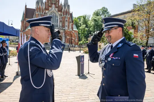 Dwaj policjanci w mundurach składają sobie salut przed budynkiem z czerwonej cegły.