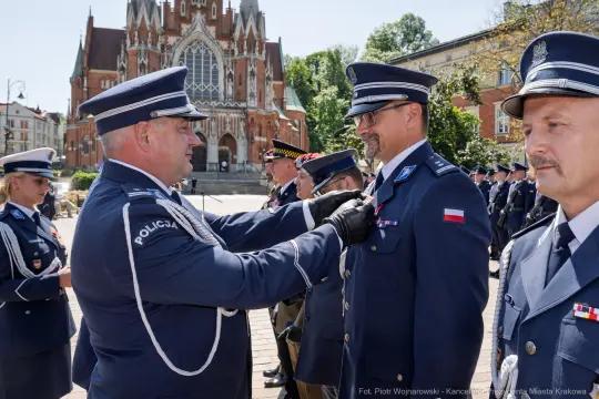 Ceremonia wręczenia odznaczeń policjantom na tle budynku w Krakowie.