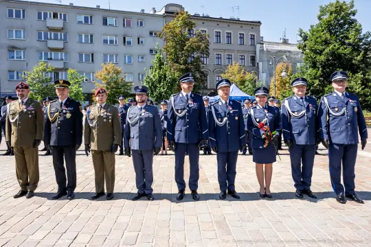 Ceremonia wojskowa z uczestnikami w mundurach, odznaczeniami i kwiatami.