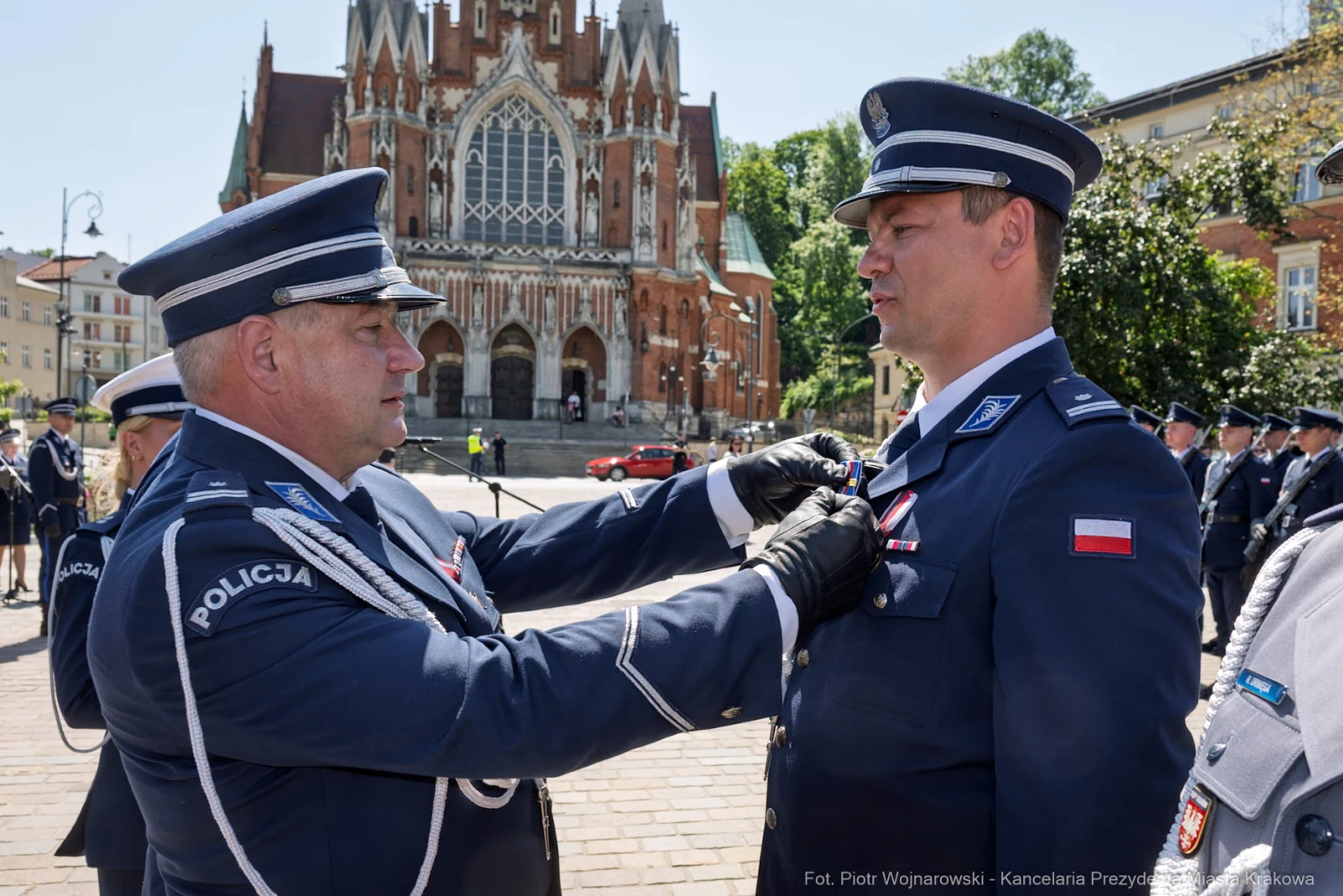 Ceremonia wręczenia odznaczenia policjantowi przed budynkiem w stylu neogotyckim.  Autor: Piotr Wojnarowski