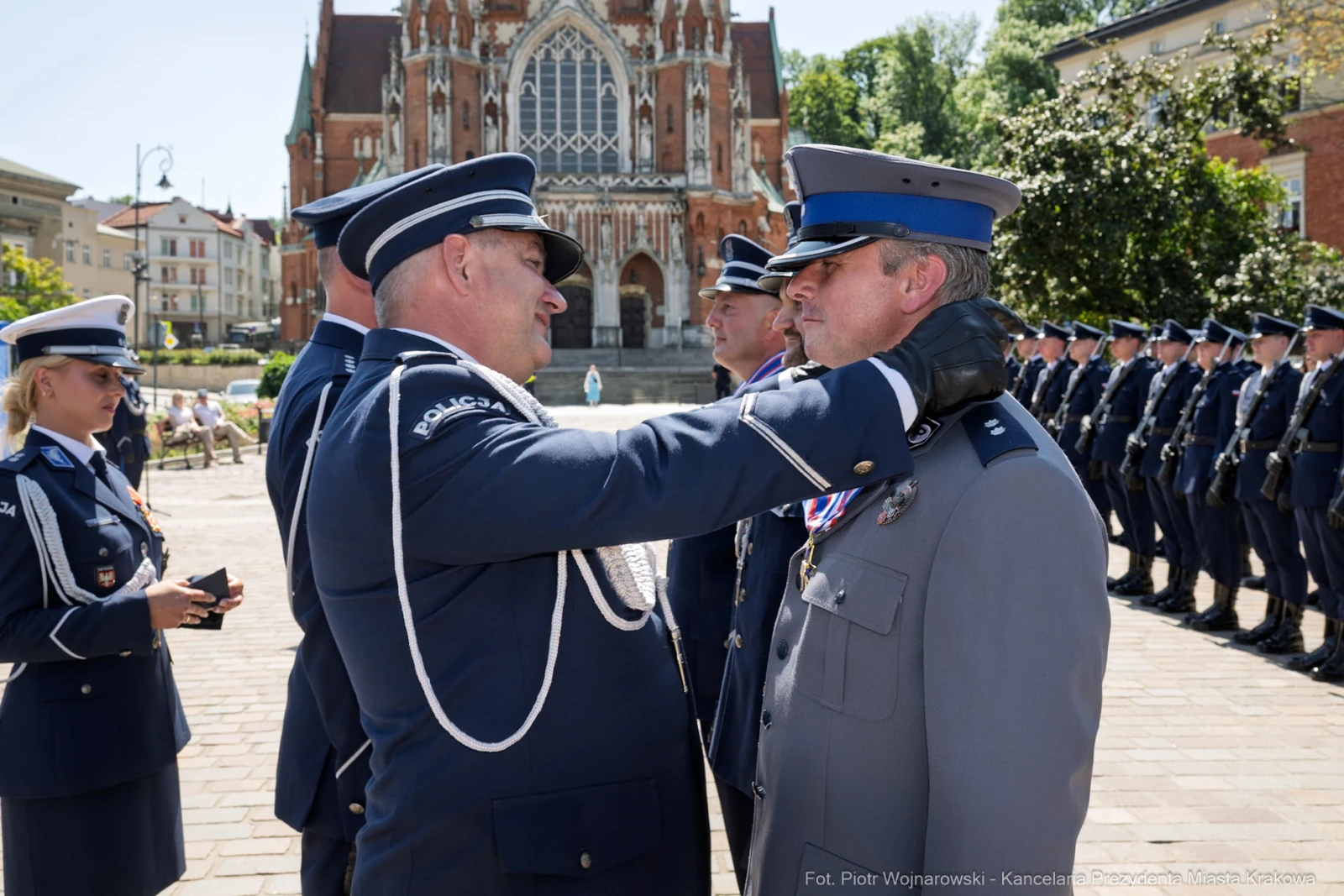 Ceremonia wręczenia odznaczeń w obecności policjantów i budynku w tle.  Autor: Piotr Wojnarowski