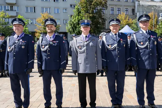 Czterech mężczyzn w mundurach policyjnych z medalami, stojących w szeregu na tle budynków.