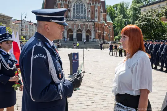 Spotkanie przedstawicieli policji z kobietą na tle budynku i zgromadzenia mundurowych.