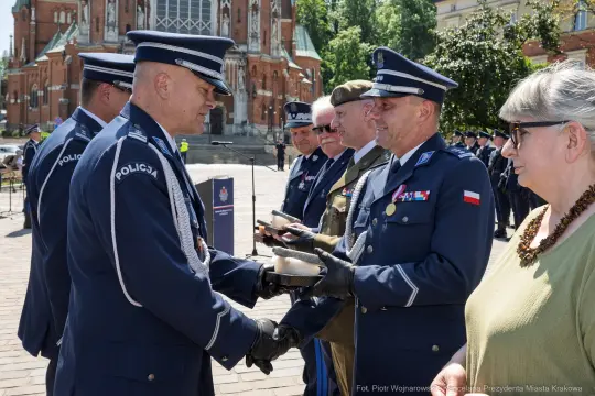 Ceremonia wręczenia odznaczeń policjantom w plenerze, z widokiem na zabytkowy budynek.