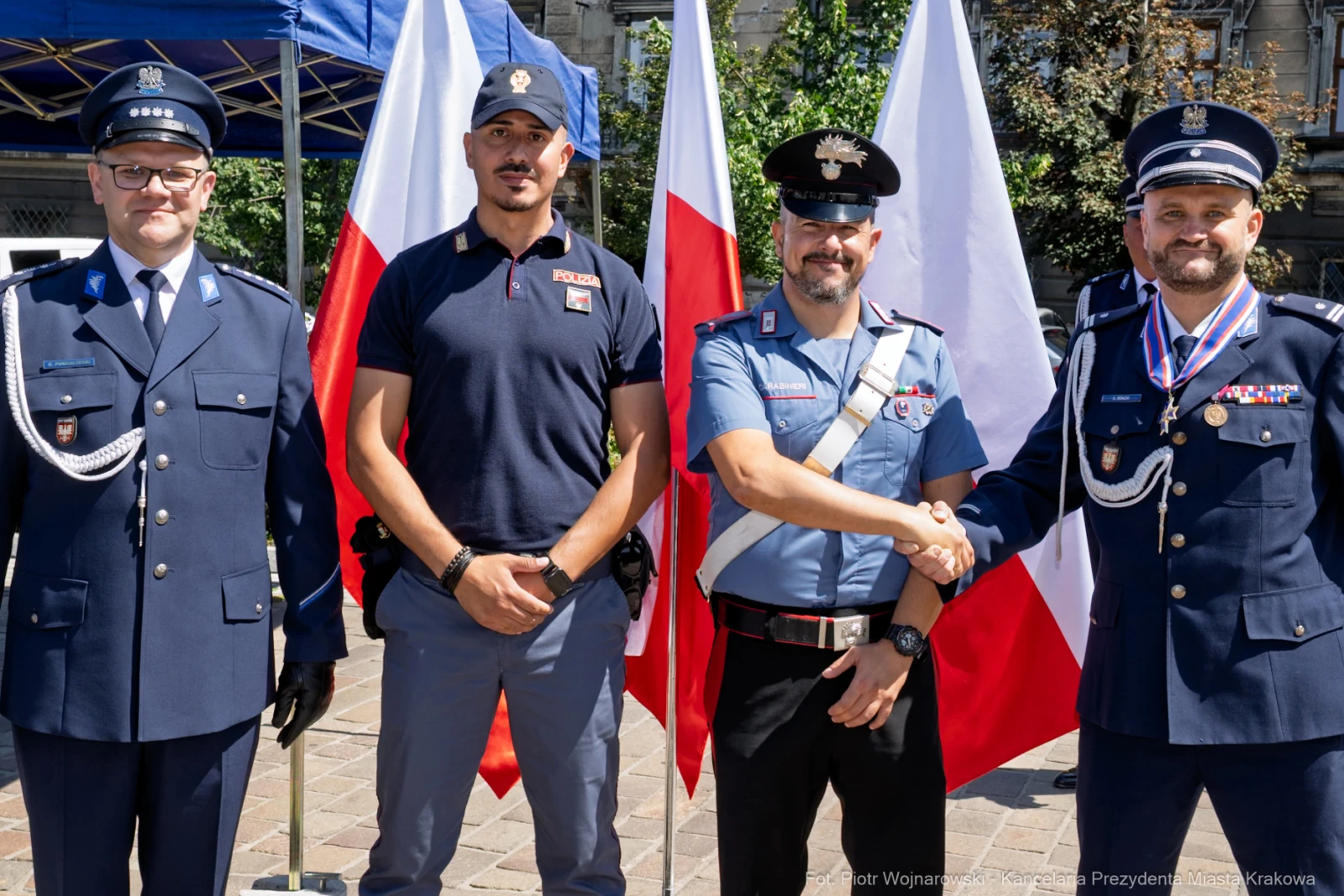Czterech mężczyzn w mundurach, stojących obok siebie, z flagami Polski w tle.  Autor: Piotr Wojnarowski