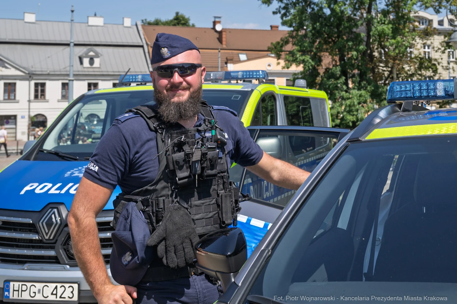 Policjant w mundurze stoi obok radiowozu, uśmiechając się do kamery.  Autor: Piotr Wojnarowski