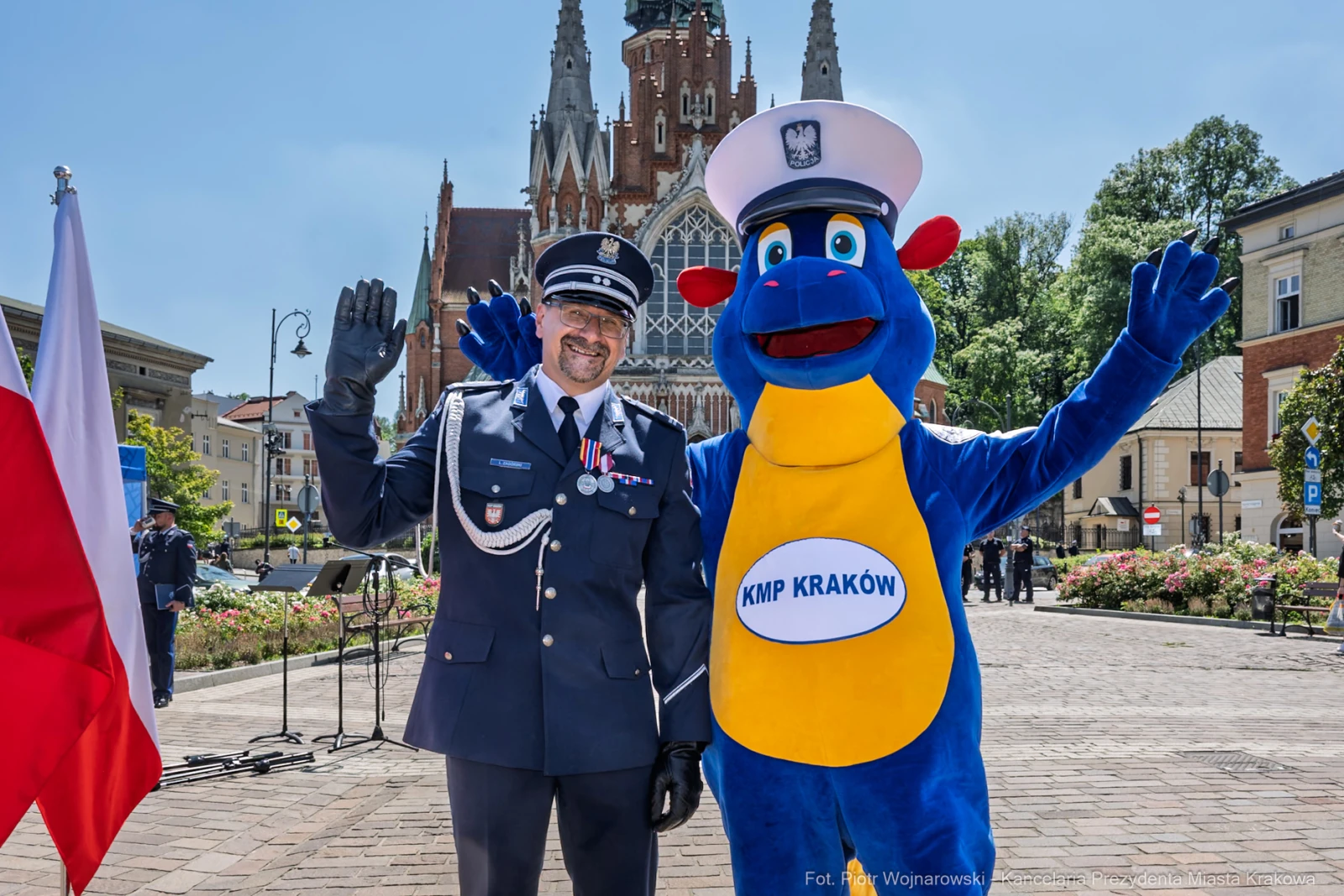 Policjant w mundurze i maskotka KMP Kraków pozują na tle zabytkowego budynku.  Autor: Piotr Wojnarowski