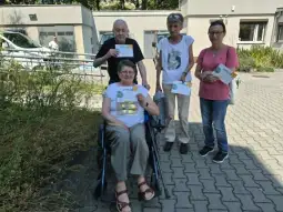 Cztery osoby, w tym jedna na wózku inwalidzkim, trzymają dyplomy w ogrodzie.