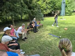 Grupa osób siedzących na ławkach w parku, obserwujących grę w kółko.